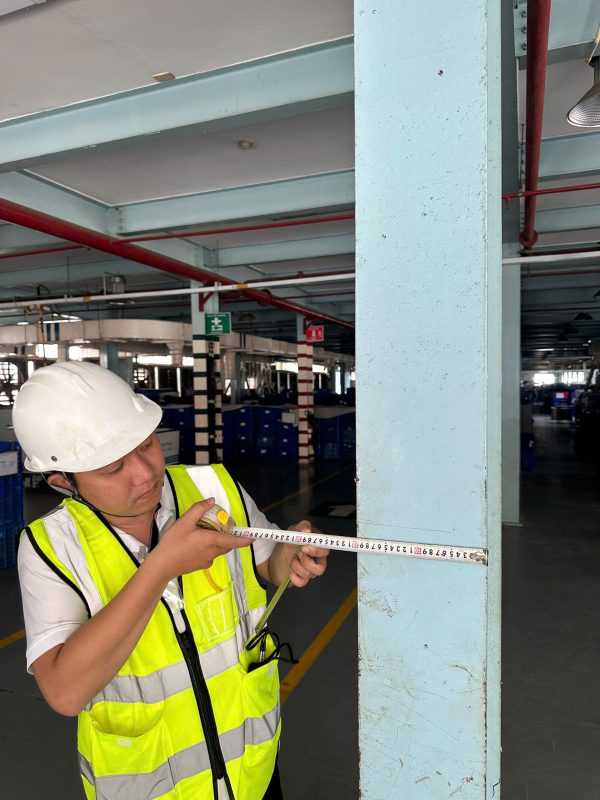 Kỹ sư kiểm định đo đạc kích thước và khoảng cách cột nhà xưởng tại hiện trường.