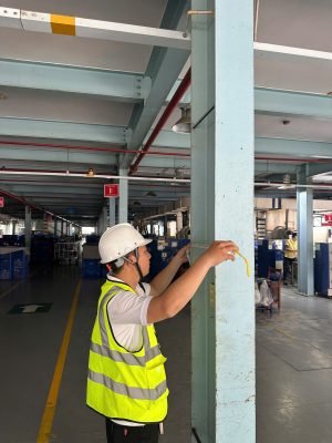 Kỹ sư kiểm định đo khoảng cách giữa các cột kết cấu nhà xưởng tại hiện trường.