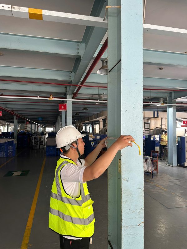 Kỹ sư kiểm định đo khoảng cách giữa các cột kết cấu nhà xưởng tại hiện trường.
