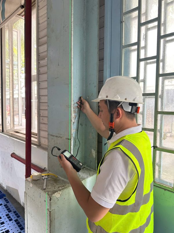 Kỹ sư kiểm định đo đạc kích thước ô cửa và tường bao nhà xưởng tại hiện trường.