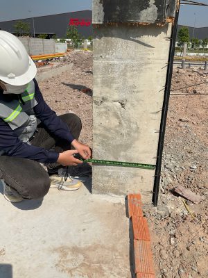 Kỹ sư kiểm định an toàn chịu lực đo kiểm vị trí và khoảng cách cột bê tông tại công trình.